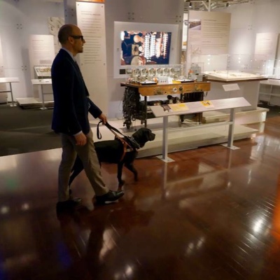 A visitor walking the Computer History Museum galleries with a guide dog during the AI-guided tour